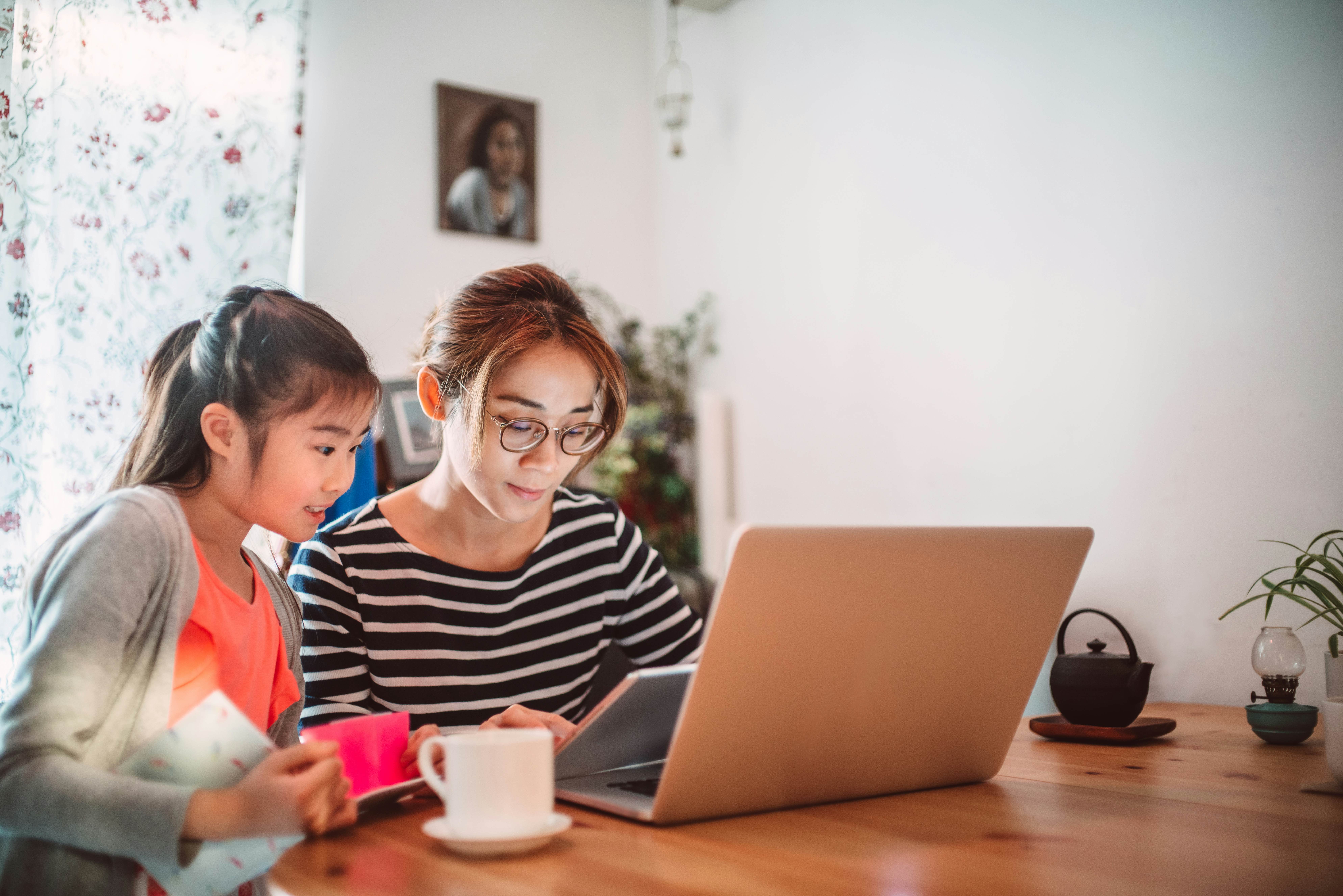 Lovely girl reading e-learning resources on the laptop computer with the assistance of her mom at home